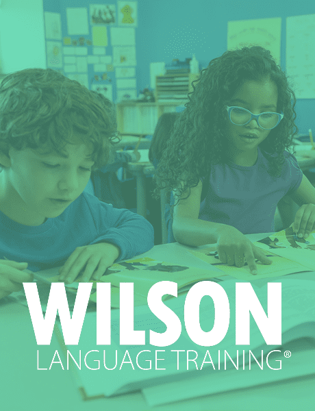 Two young students sitting at a classroom table reading books, with the Wilson Language Training logo overlaid in white text.