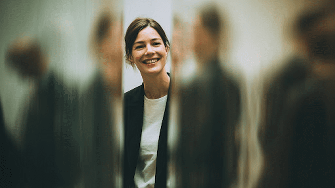 A smiling woman in a blazer stands in a blurred hallway, embodying the "Dreamwriter" concept.
